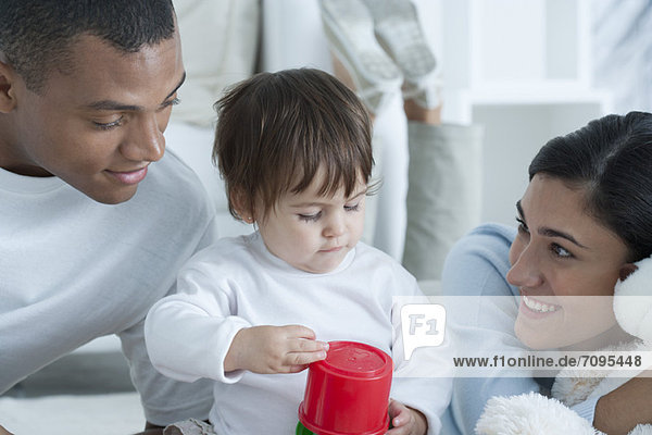 Young parents watching baby girl play with toy
