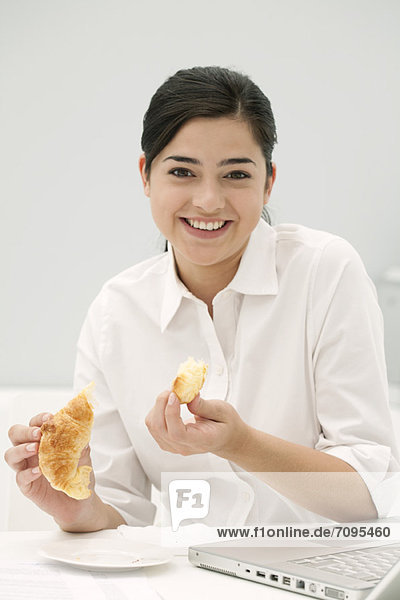 Young woman eating croissant  smiling