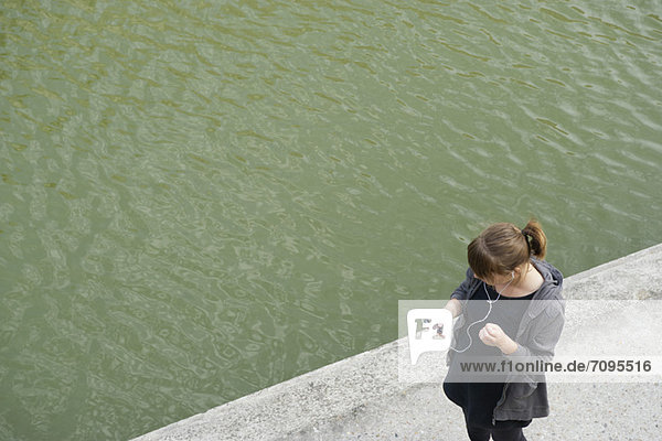 Junge Frau geht am Kanal entlang  hört MP3-Player  erhöhte Ansicht