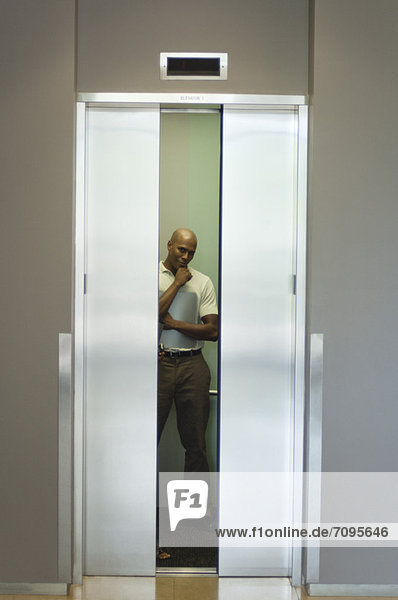Junger Mann im Aufzug stehend mit Hand unter dem Kinn  Türen schließend