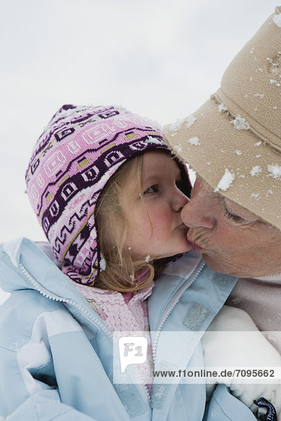 Kleinkind Mädchen küsst Großmutter im Schnee