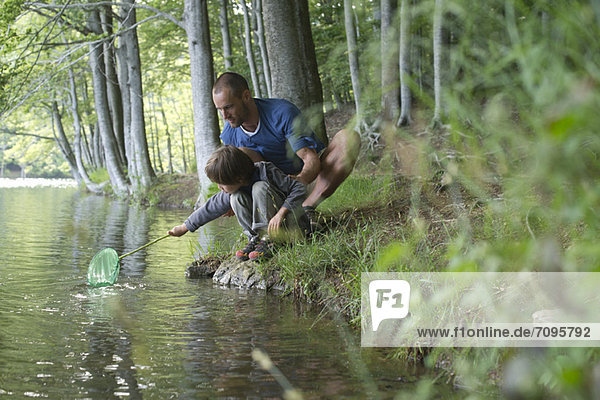 Vater und Sohn hocken am Ufer mit Fischernetz