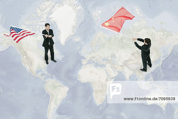 Geschäftsleute  die auf der Weltkarte stehen und amerikanische und chinesische Flaggen schwenken.