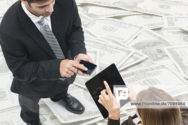 Executives exchanging information on wireless devices  pile of money in background