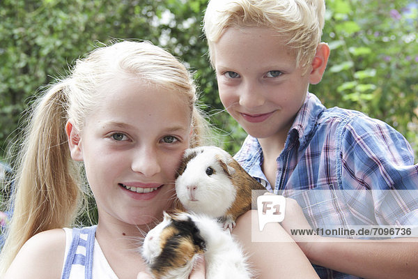 Girl and boy holding guinea pigs