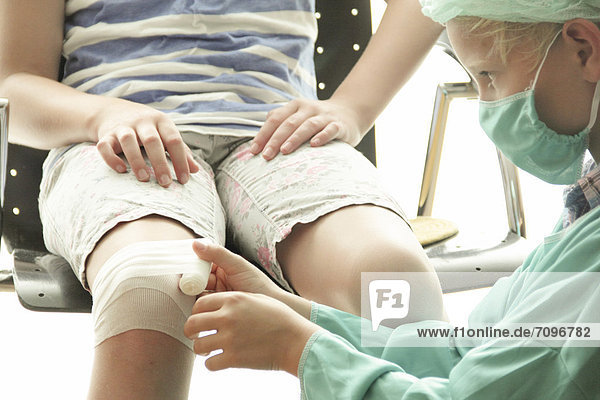 Mädchen und Junge spielen Arzt  Junge als OP-Arzt verkleidet verbindet das Knie des Mädchens