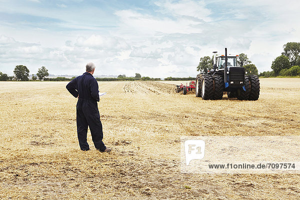 Farmer overlooking tractor in crop field