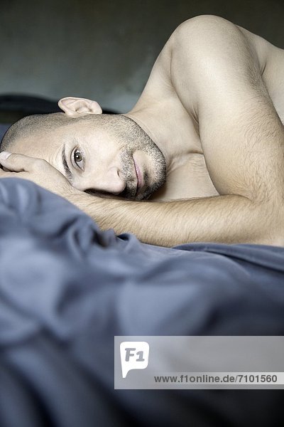 Barechested man with designer lying in bed