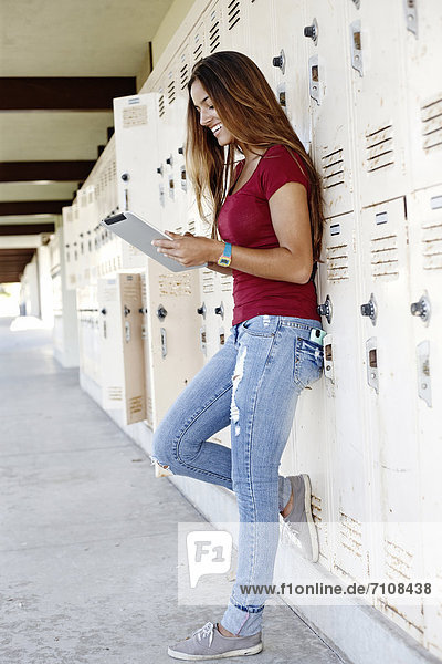 Caucasian teenager leaning on lockers using digital tablet