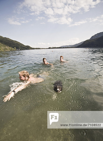 Caucasian friends swimming in lake with dog