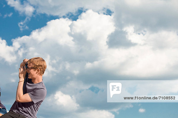 Junger Mann fotografiert mit Wolken am Himmel