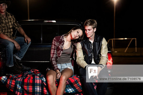 Paar sitzt nachts auf der Heckklappe des Autos