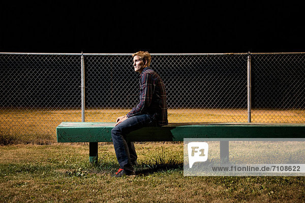 Nachdenklicher junger Mann  der nachts auf der Tribüne sitzt.