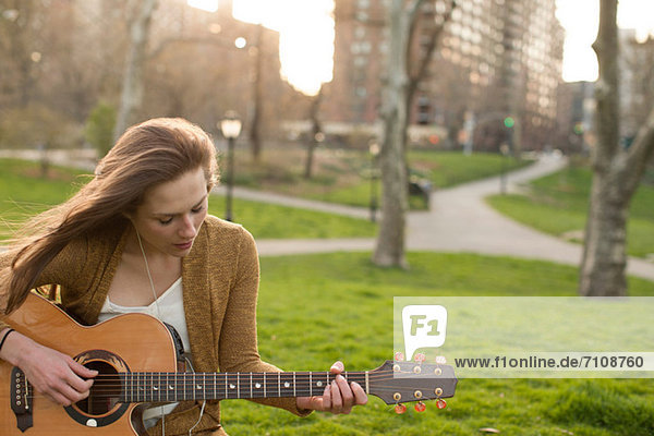 Junge Frau spielt Gitarre im Park