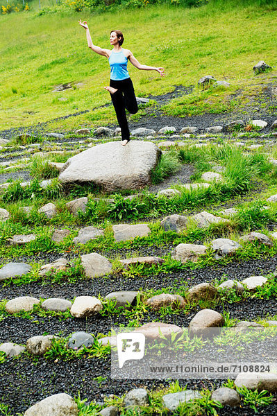 Frau in Yoga-Pose auf Stein im Labyrinth