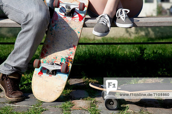 Young couple on bench with skateboards  low section