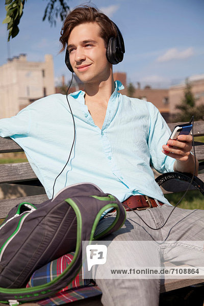 Young man sitting on bench listening to music