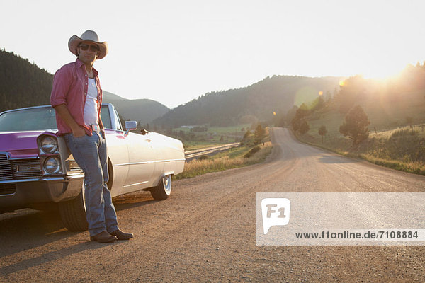Man in cowboy hat  leaning against convertible car