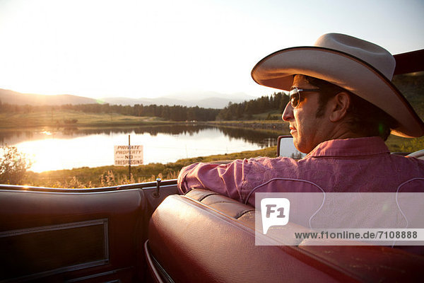 Man in cowboy hat  looking at lake from his car