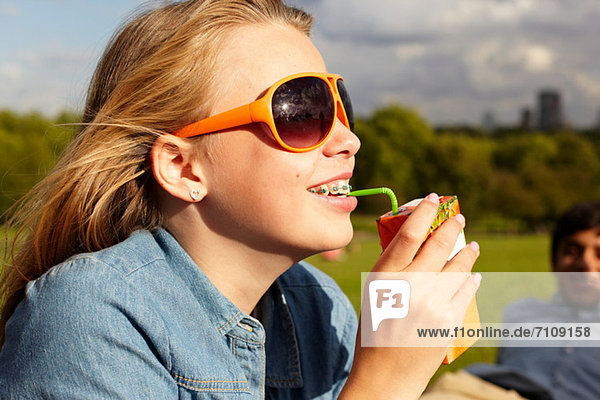 Teenagermädchen in Sonnenbrille trinkt aus Saftkarton