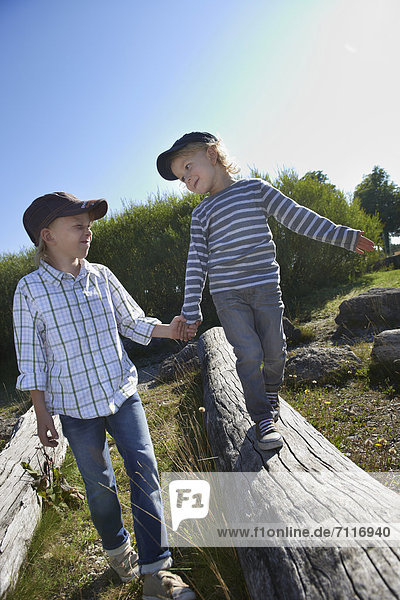 Kinder helfen sich beim Balancieren auf Baumstamm