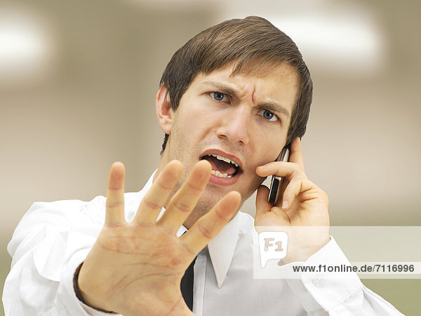 Aggressive businessman speaking on his mobile phone  portrait  stressed  defensive gesture