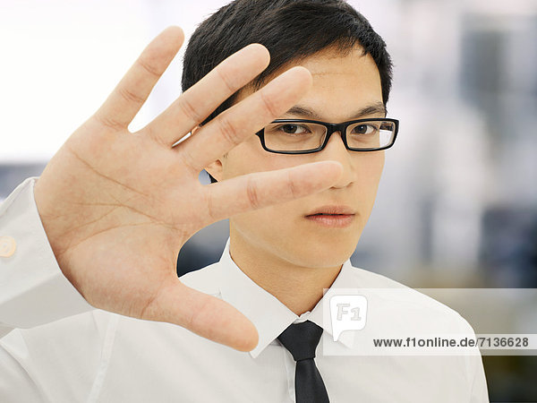 Junger Geschäftsmann  Asiate  mit Brille  hält Hand vor Gesicht  abweisend  ernst  gestresst