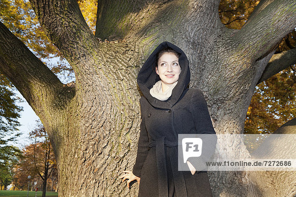 Junge Frau mit Kapuzenmantel an einem Baum