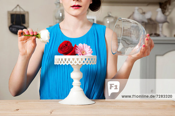 Frau hebt den Deckel des Kuchenständers mit Blumen ab