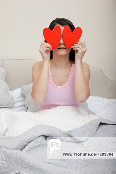 Woman in bed holding heart shapes over eyes