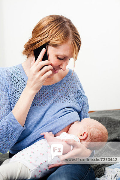 Mother on phone breast feeding newborn daughter