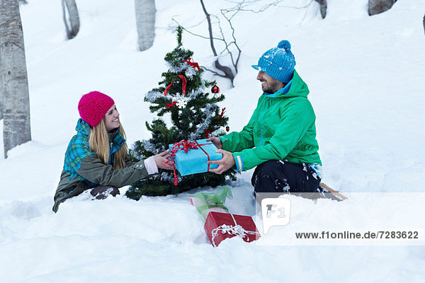 Paar sitzend am Weihnachtsbaum mit Geschenken