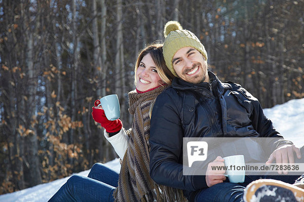 Portrait of couple sitting in snow with hot drinks