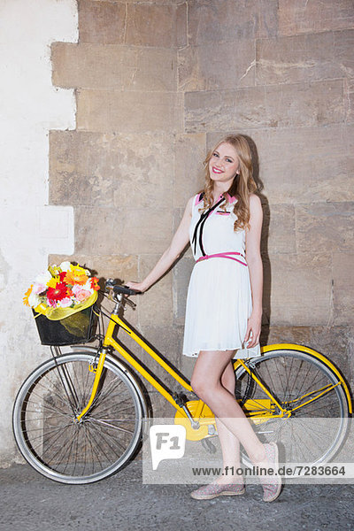 Young woman with flowers in basket of bicycle