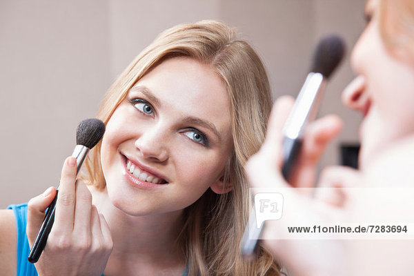 Young woman applying blusher in the mirror