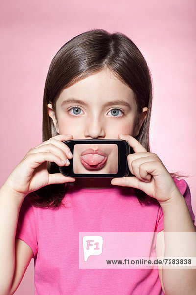 Mädchen hält Smartphone über den Mund  streckt Zunge heraus