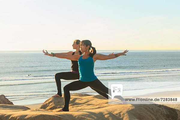 Two women practising yoga on beach