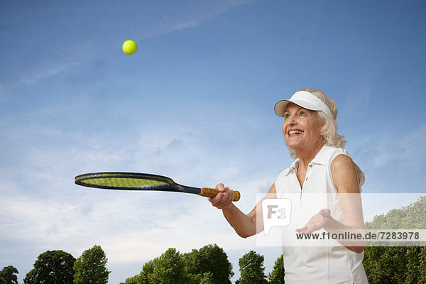 Seniorenfrau hüpfend Tennisball auf Rakete