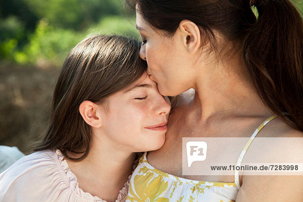 Porträt der Mutter  die die Tochter auf die Stirn küsst