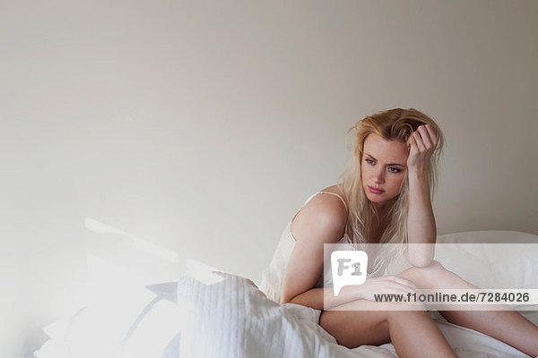 Verärgerte junge Frau auf dem Bett sitzend