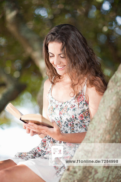 Woman reading book in tree outdoors