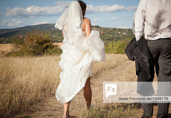 Neuvermählte Braut hält Kleid im Gras hoch
