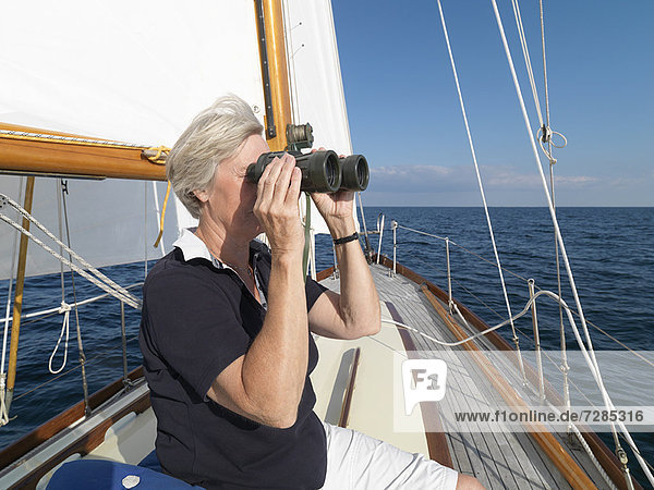 Older woman using binoculars on sailboat