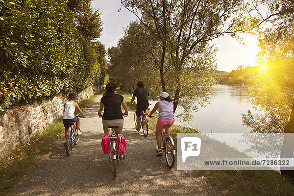 Family riding bicycles by river bank