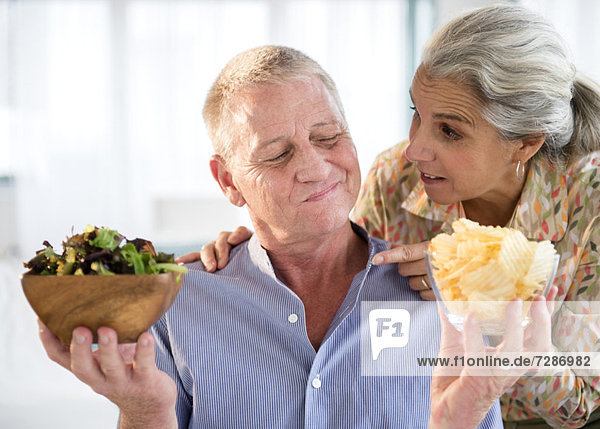 Elderly couple choosing between fresh salad and crisps