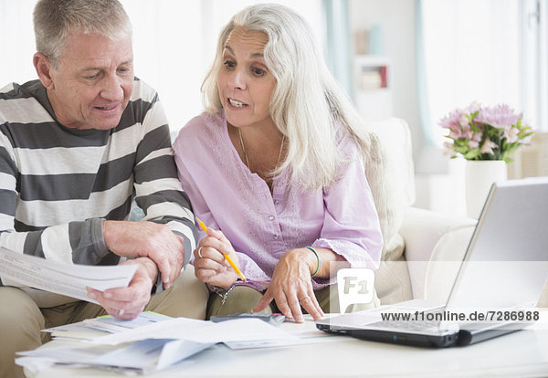 Elderly couple with laptop and documents sitting in living room