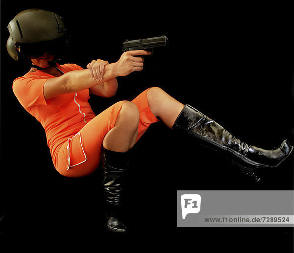 Frau in orangem Overall schießt im Fallen mit Pistole