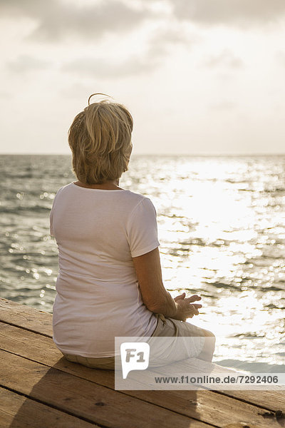 Spain  Senior woman sitting on jetty at the sea