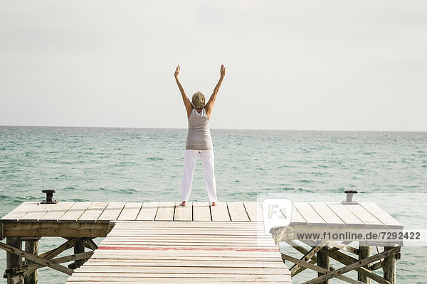 Spain,  Senior woman exercising on jetty at the sea