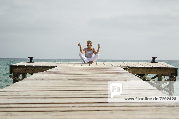 Spain,  Senior woman doing yoga on jetty at the sea